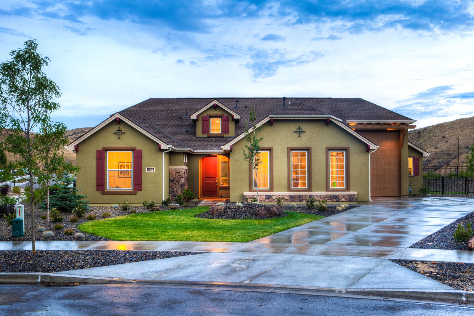 A St. George home at dusk with a manicured green lawn, desert rock-mulch planting beds, and red-rock hills behind